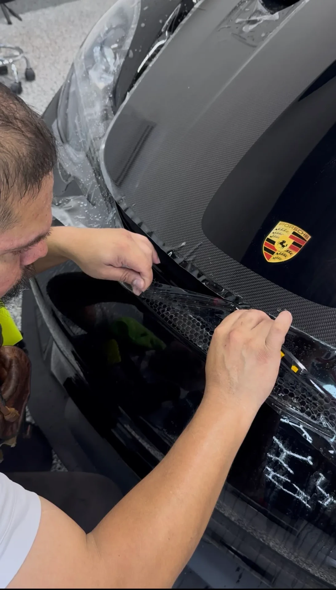 Technician finishing PPF near a Porsche front grille