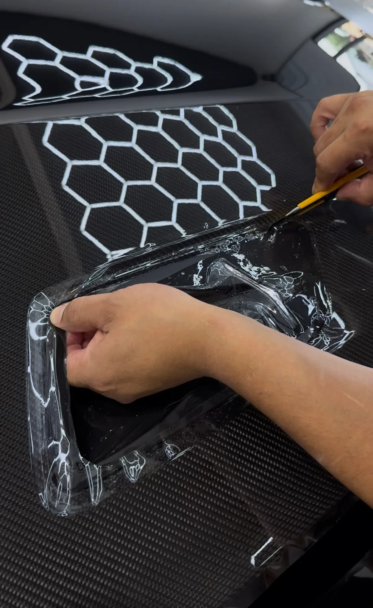 Technician trimming clear paint protection film around a vehicle detail