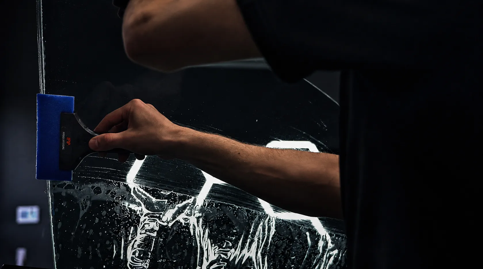 Huracán Nero technician installing window tint on a windshield under studio lights