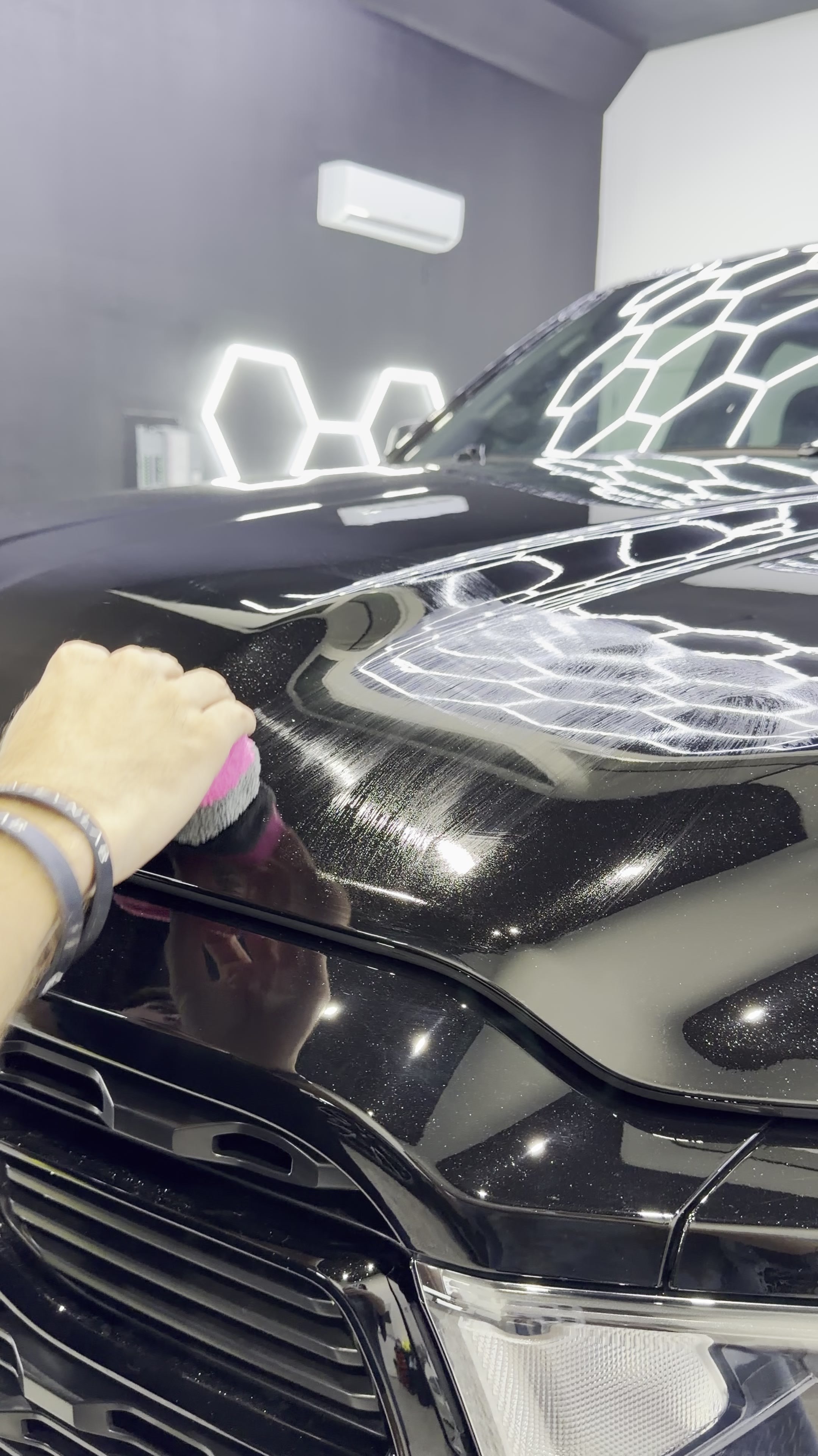 Ceramic coating being hand-applied to glossy black paint under studio lights